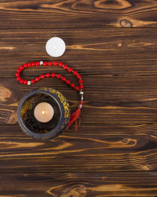 Chapelet de prière rouge et bougie allumée sur une table en bois