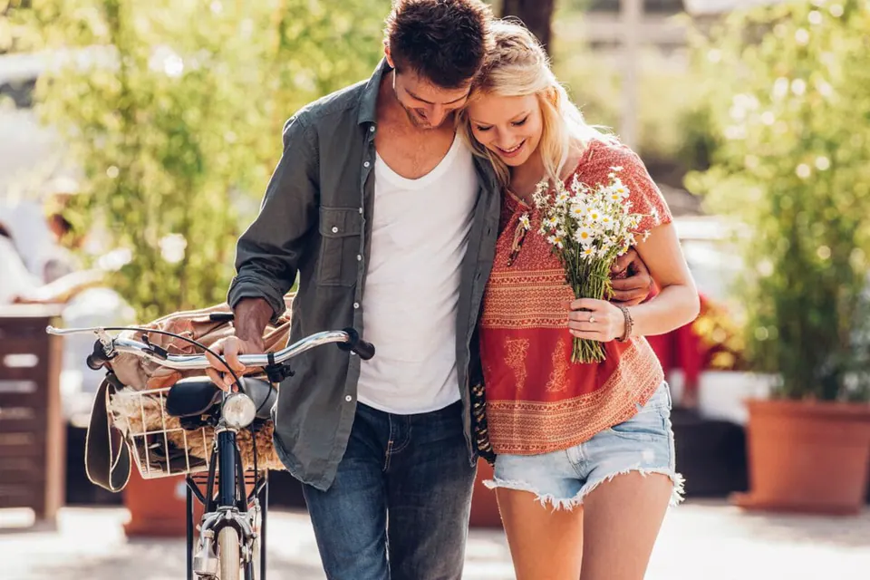 Couple souriant qui marche côte à côte, un vélo à la main et un bouquet de fleurs