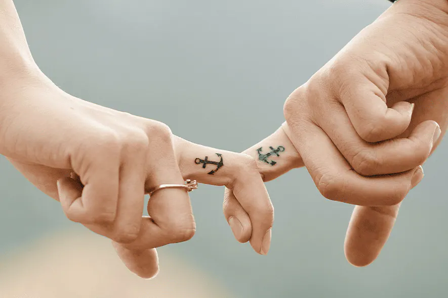 Deux mains entrelacées portant le même tatouage d'ancre