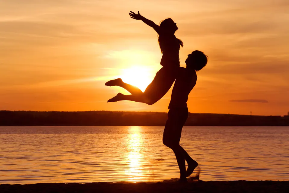Silhouettes d'une femme qui saute dans les bras d'un homme au coucher du soleil, au bord de l'eau